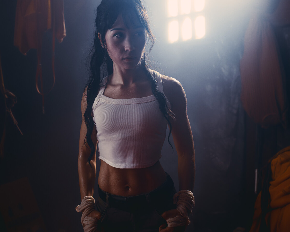 A woman standing in a dim room with light streaming through a window behind her